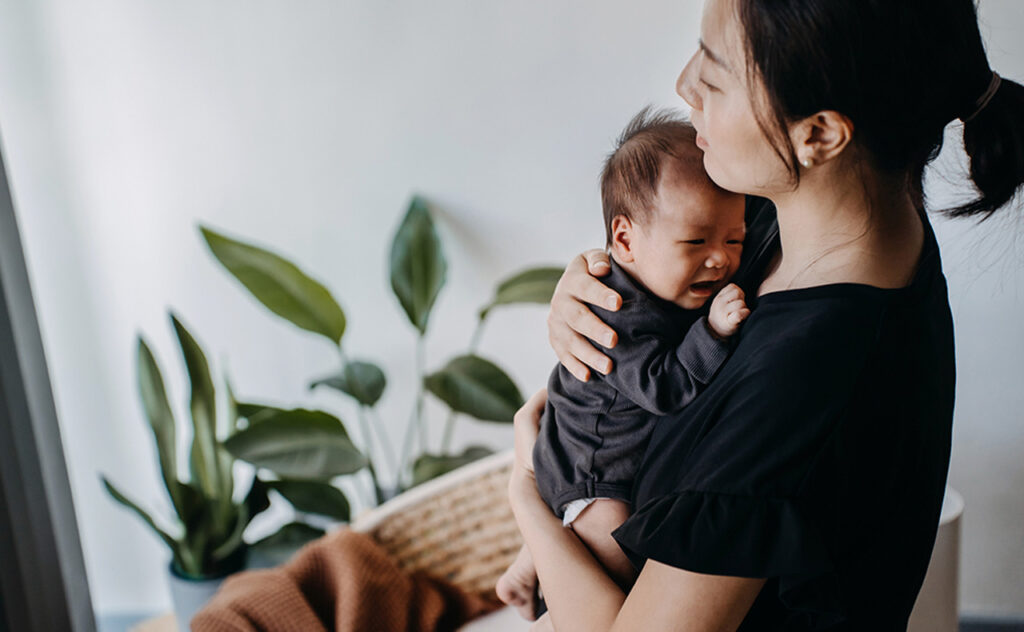 A loving young Asian mother carrying her newborn baby girl in arms, consoling and comforting her crying baby. Hunger and discomfort. Love and care. 