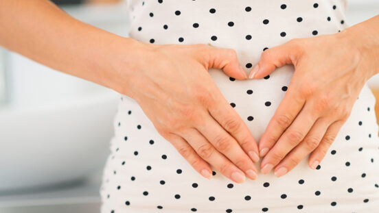 Closeup on young woman holding hands in heart shape on her belly