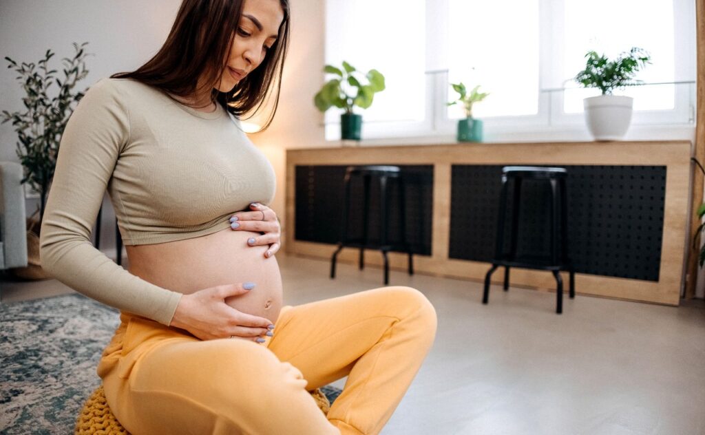 Young happy pregnant woman is sitting on the floor in the living room