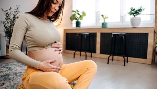 Young happy pregnant woman is sitting on the floor in the living room