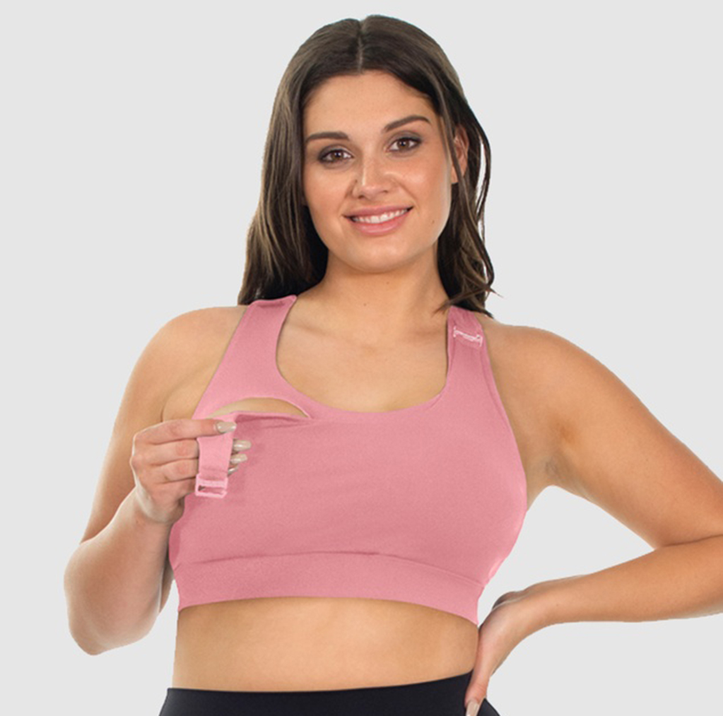 Pregnant woman with dark hair smiling at the camera holding the drop-down strap of a pink B Free Maternity & nursing mesh racer back sports bra