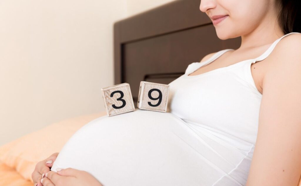 Pregnant woman in white underwear on bed in home holding calendar with weeks 39 of pregnant.