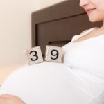 Pregnant woman in white underwear on bed in home holding calendar with weeks 39 of pregnant.