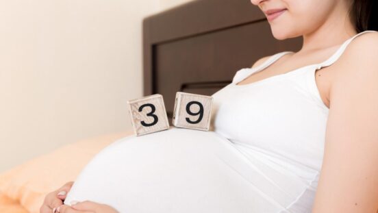 Pregnant woman in white underwear on bed in home holding calendar with weeks 39 of pregnant.