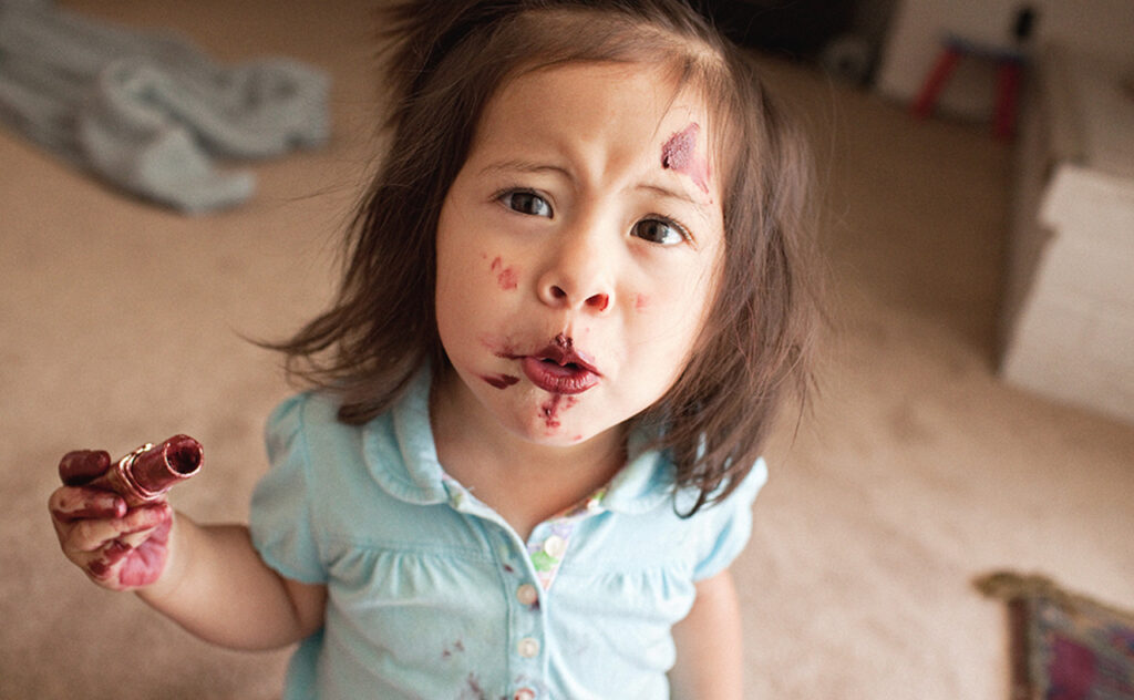 Toddler girl smeared her face with tube of lipstick.