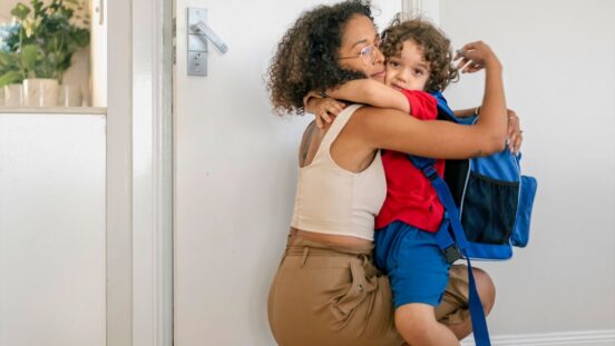 Mixed race mother hugs her young son tightly. He is dressed and getting ready for his first day back to school.