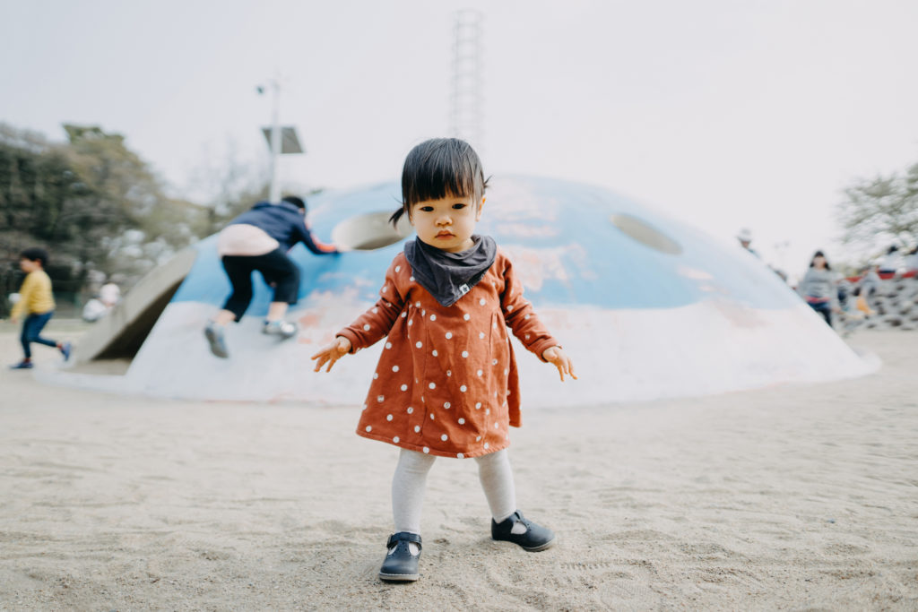 A happy, smiling cute Asian toddler girl having fun in outdoor sand playground