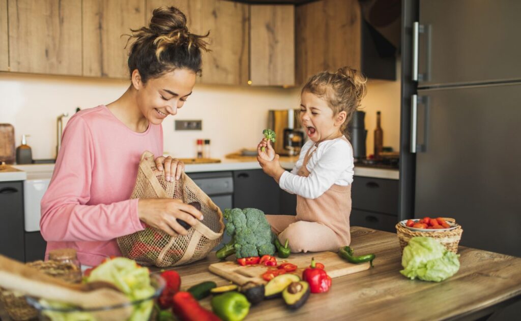 Mother and daughter preparing fresh vegetables for cooking at kitchen. Both laughing 