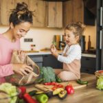 Mother and daughter preparing fresh vegetables for cooking at kitchen. Both laughing