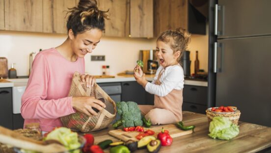 Mother and daughter preparing fresh vegetables for cooking at kitchen. Both laughing