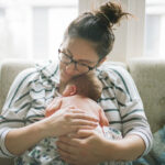 A mother holds her newborn baby boy close to her chest while seated and resting on a white sofa.