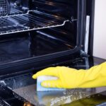 Close up of female hand with yellow protective gloves cleaning oven door