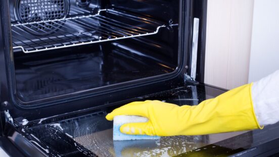 Close up of female hand with yellow protective gloves cleaning oven door