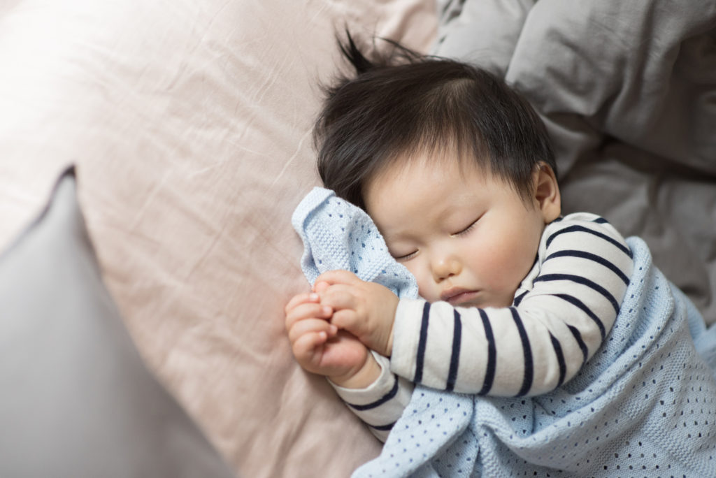 Older Asian baby cuddled in a blanket, sleeping on their side with their hands out in front of them