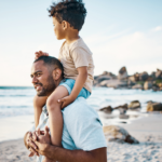 Dark haired dad on the beach with his dark hair young son on shoulders