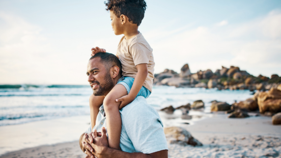 Dark haired dad on the beach with his dark hair young son on shoulders