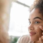 Mixed Race woman applying lotion to cheek