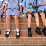 three smiling children in school uniform in front of a brick wall