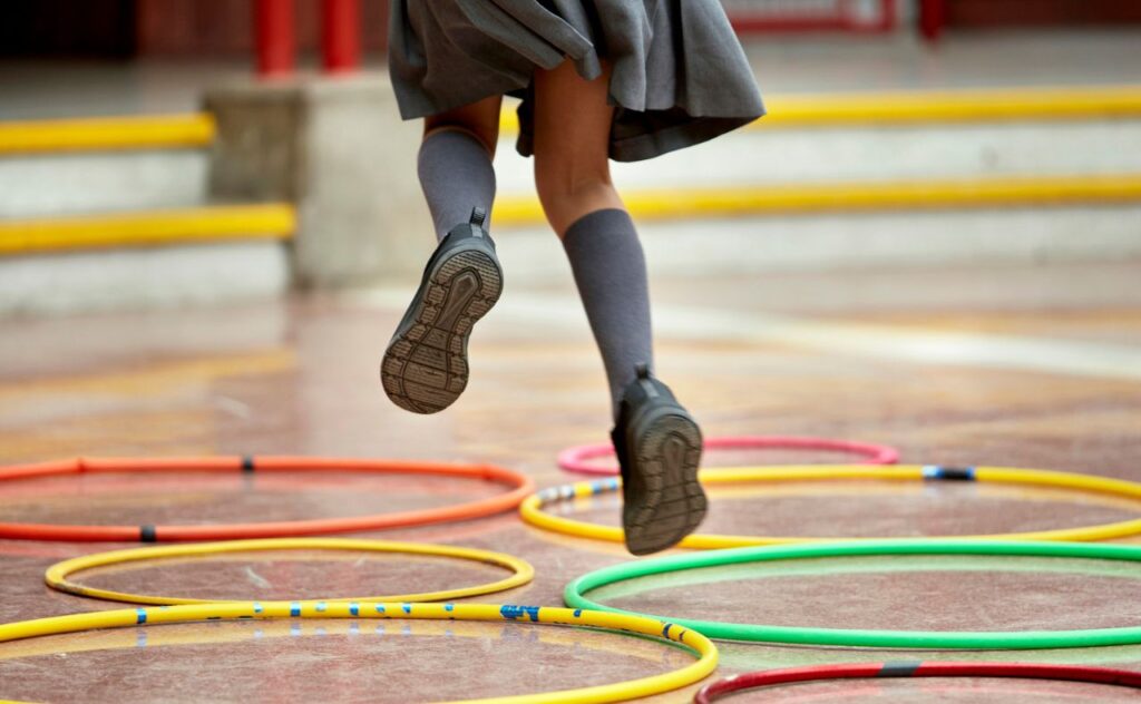 Little girl in school uniform jumping through hoops