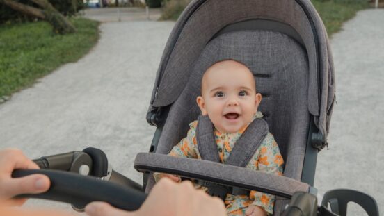 Cute bald baby smiles up from an affordable stroller, looking toward the person pushing them