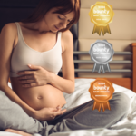 Pregnant woman sitting on a bed, wearing a white maternity crop bra agrey track pants social