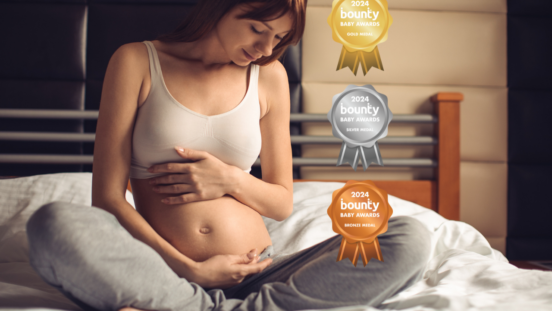 Pregnant woman sitting on a bed, wearing a white maternity crop bra agrey track pants social