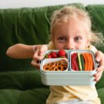 Girl on sofa showing her bento box with fruit and vegies