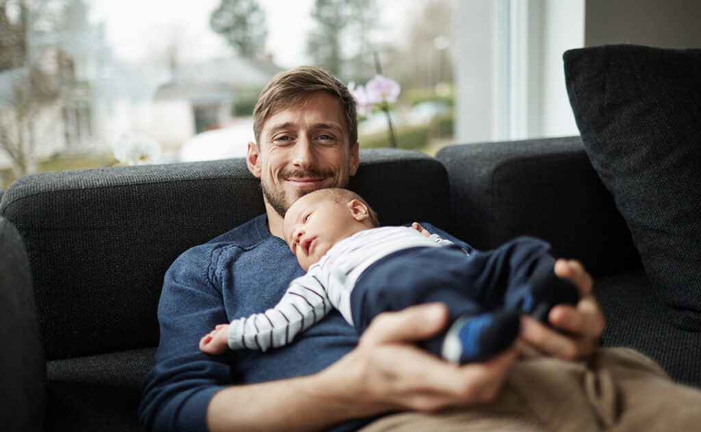 Smiling father and baby boy lying on couch.