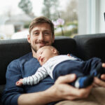 Smiling father and baby boy lying on couch.