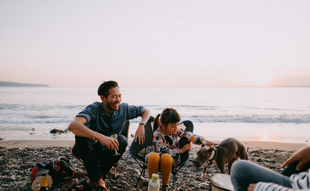 Japanese father and preschool mixed race girl camping at beach with dog.