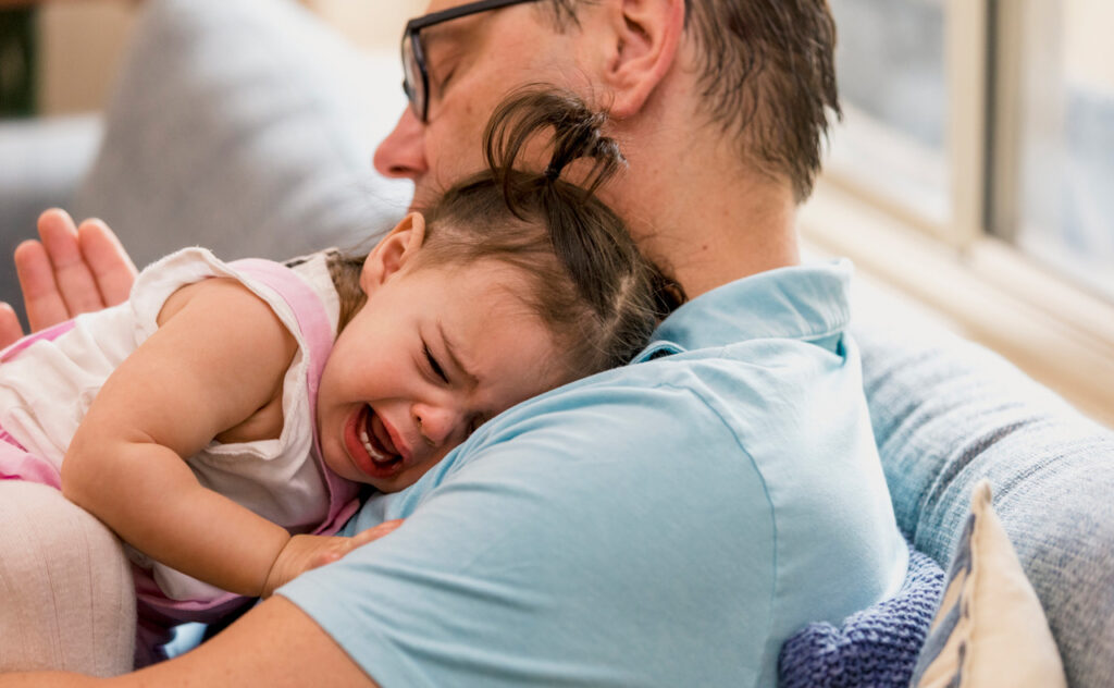 A grandfather looks in despair as his granddaughter gets upset and his crying in his home.
