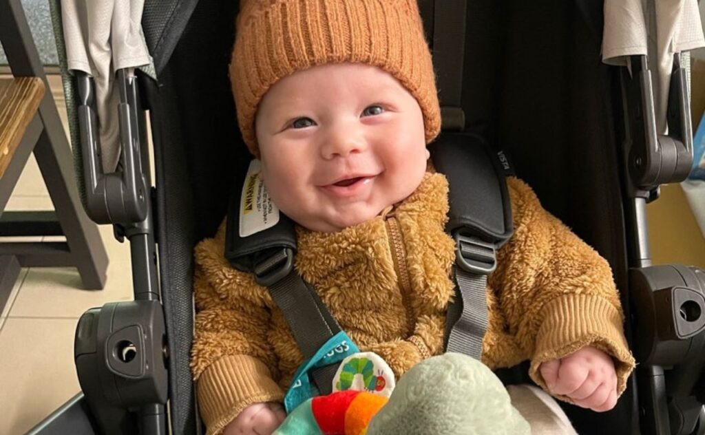 Sam Frost's son Ted smiling and rugged up in his stroller