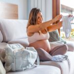 Pregnant woman folding baby clothes while packing hospital bag