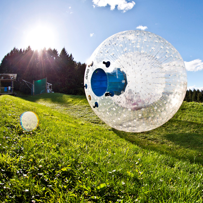 A zorb bowl rolls down a grassy hill on a summer day at ZORB Rotorua in New Zealand's North Island