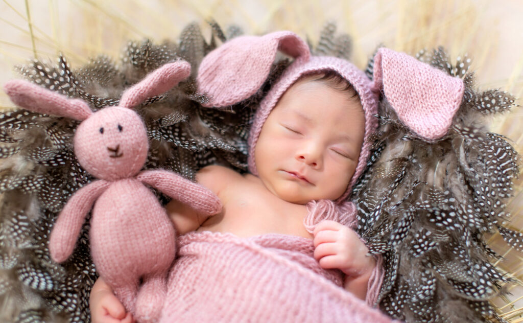 Sleeping newborn in lavender coloured woollen bunny ear bonnet and blanket.