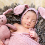 Sleeping newborn in lavender coloured woollen bunny ear bonnet and blanket.