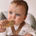 Small baby in high chair eating a rusk