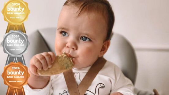 Small baby in high chair eating a rusk