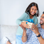 Portrait of a loving girl giving a gift to her father at home. Could be Fathers day or his birthday. They are both happy, laughing and smiling