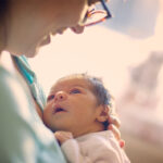 Newborn baby resting on mothers chest and staring up adoringly at mother.