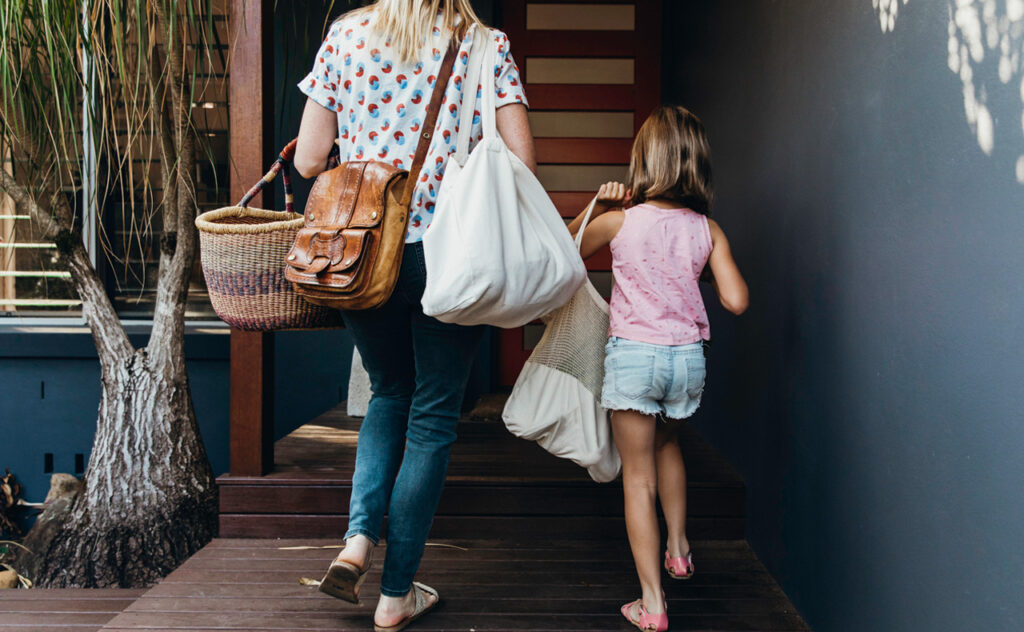 Real life young Australian mum and daughter bring in their groceries in eco shopping bags and basket
