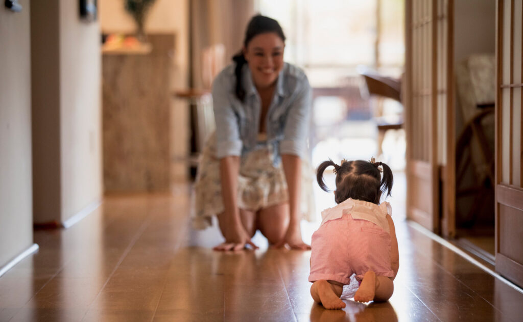 Young girl crawling along a hallway towards her mother.
