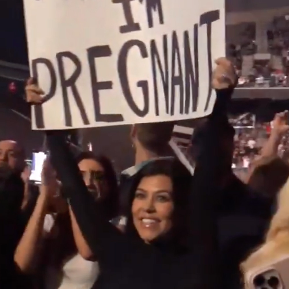 Pregnant Kourtney Kardashian Barker holds up "Travis I'm Pregnant" sign at a Blink 182 concert.