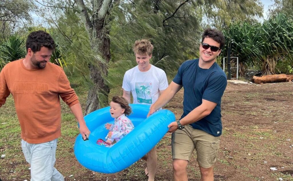 Grace being carried in a blue paddling pool by dad Chandler, uncle Robert and friend 