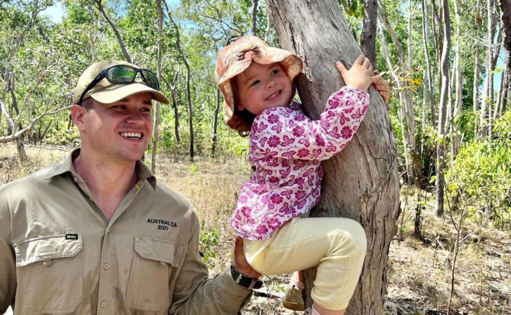 Grace holding on to a tree like a koala as dad Chandler helps hold her there