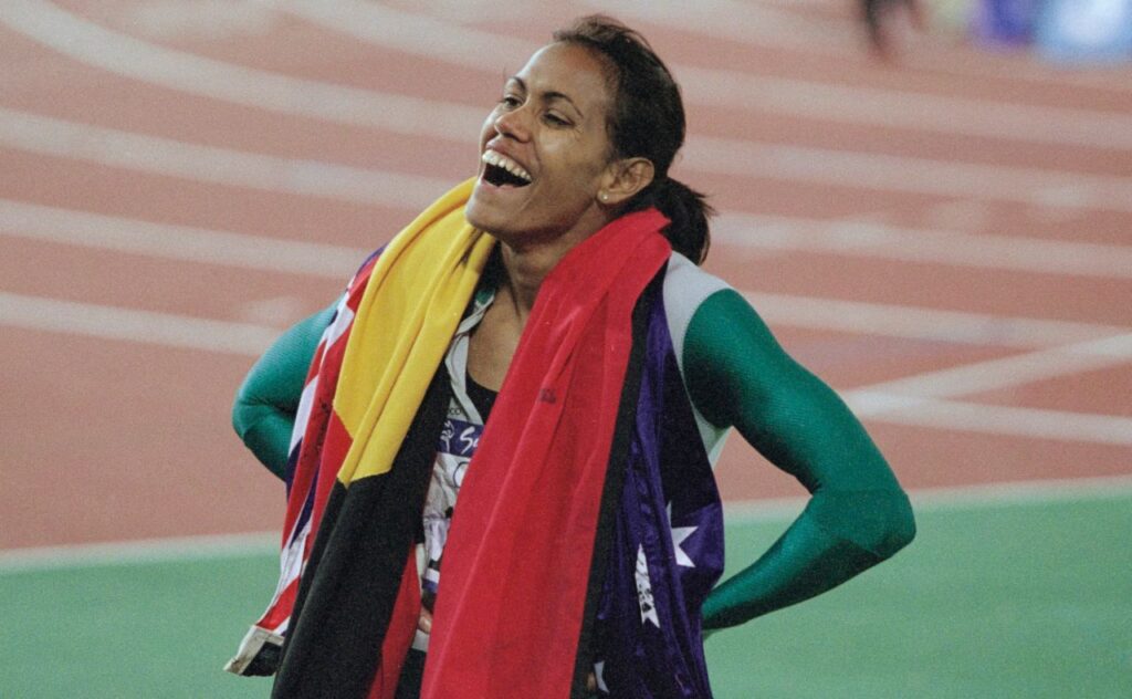 Cathy Freeman, the Australian flag and the Australian Aboriginal flag draped around her shoulders, after winning the women's 400 metres event of the 2000 Summer Olympics