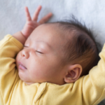 Sleeping Asian baby wearing yellow sleeves, arms up by their head