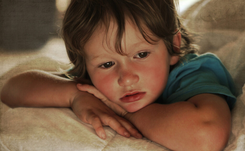 Unwell, young toddler boy lies in bed recovering from illness.