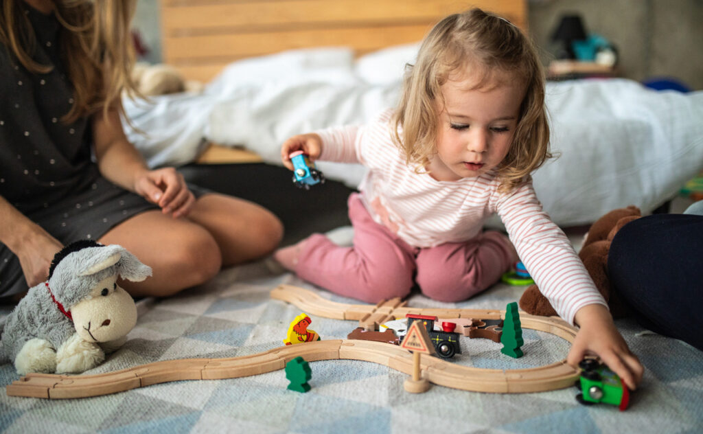 Mum playing trainset with toddler girl.