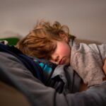 Curly haired toddler boy lying down and sleeping on his dad's chest